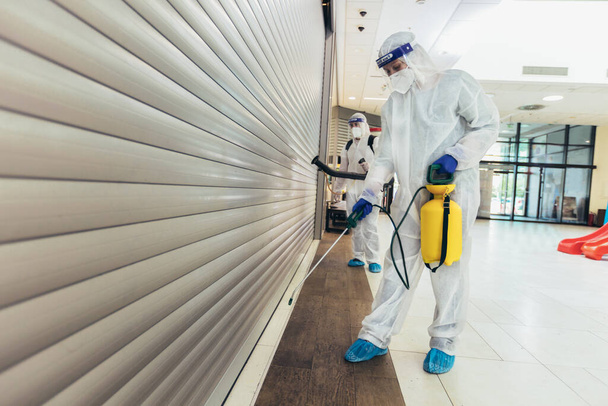 Trabajadores profesionales en trajes de materiales peligrosos desinfectando interiores de centros comerciales, riesgo pandémico para la salud, coronavirus
 - Foto, imagen