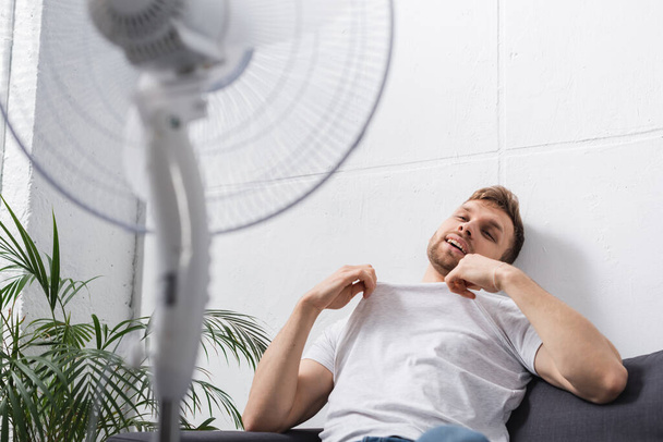 positive man feeling comfortable with electric fan at home during summer heat  - Φωτογραφία, εικόνα
