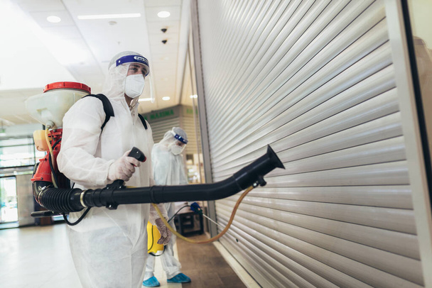 Trabajadores profesionales en trajes de materiales peligrosos desinfectando interiores de centros comerciales, riesgo pandémico para la salud, coronavirus
 - Foto, imagen