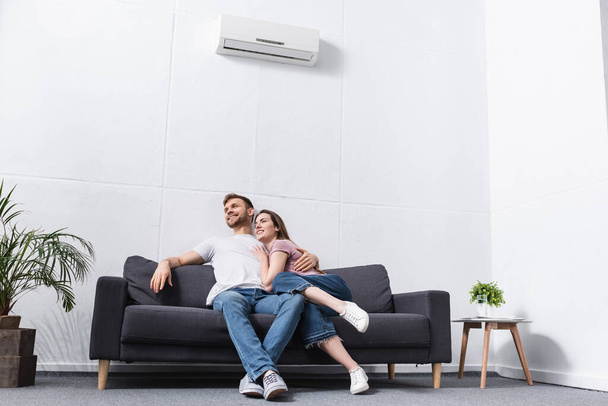 happy girlfriend and boyfriend hugging at home with air conditioner - Zdjęcie, obraz