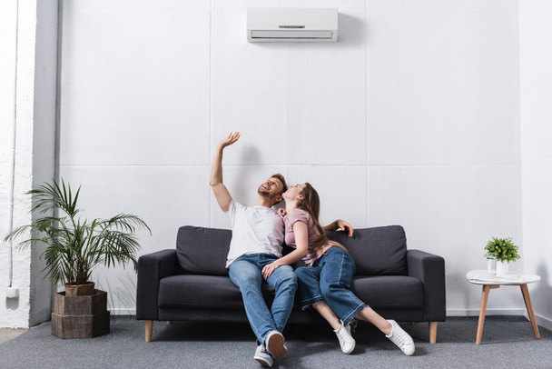 smiling girlfriend and boyfriend hugging at home with air conditioner - Φωτογραφία, εικόνα