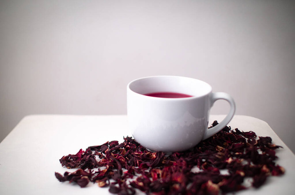 White Wooden Table with a Mug and Hibiscus Flower / Roselle (Hibiscus Sabdariffa) in a White Background - Foto, Imagem