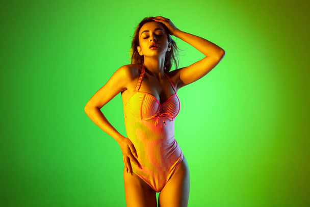 Beautiful girl in fashionable swimsuit isolated on gradient studio background in neon light. Summer, resort, fashion and weekend concept - Foto, immagini