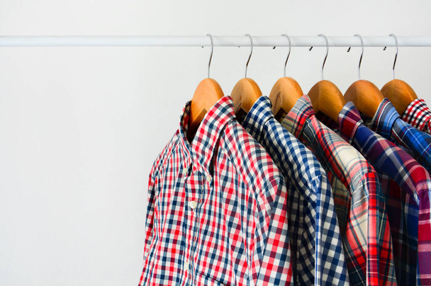 Nahaufnahme Kleider hängen auf Regal oder Kleiderständer, langärmeliges rot-blau kariertes Hemd auf Holzbügel über weißem Hintergrund, Kopierraum - Foto, Bild