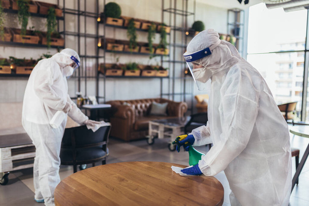Trabalhadores profissionais em ternos hazmat desinfecção interior de café ou restaurante, risco de pandemia de saúde, coronavírus
 - Foto, Imagem