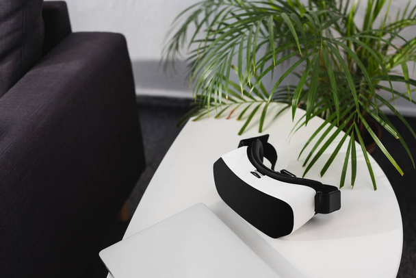 virtuális valóság headset és zárt notebook közelében zöld növény az asztalon - Fotó, kép