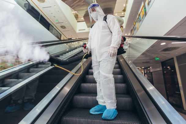 Professionele werknemers in hazmat pakken desinfecteren binnenshuis van winkelcentrum, pandemische gezondheidsrisico 's, coronavirus - Foto, afbeelding