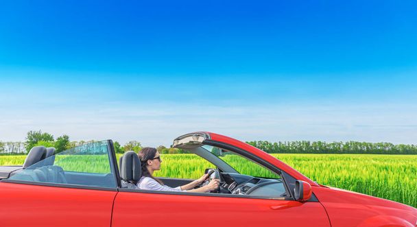 Woman in a red car against the background of a field outside the city. - Photo, Image