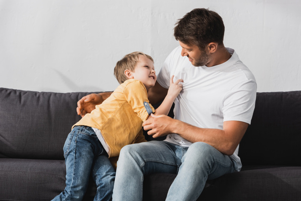 cheerful father and son having fun while jokingly fighting on sofa at home - Photo, Image