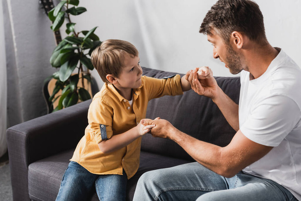 father and son holding hands and looking at each other while sitting on sofa at home - Photo, Image