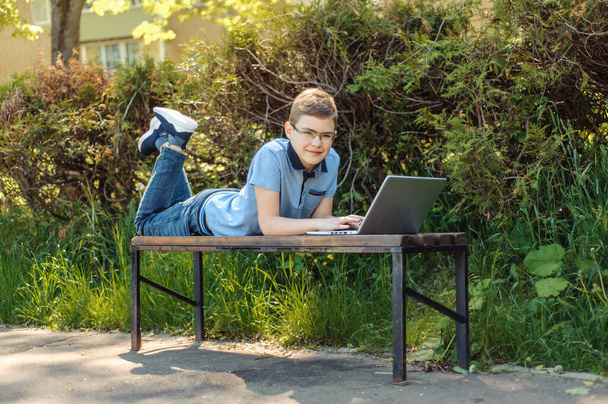 The boy learns remotely. A teenager with a laptop in the park. Keeps his distance. The boy is alone on the bench. - Foto, Imagen
