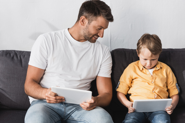 sonriente padre mirando tableta digital en manos de hijo atento
 - Foto, Imagen