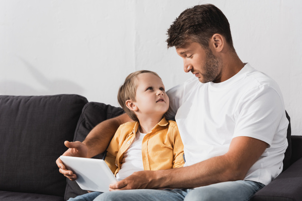 handsome father with adorable son looking at each other while using digital tablet - Fotografie, Obrázek
