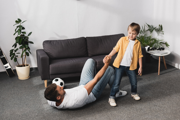 cute boy giving hand to fallen father holding soccer ball - Valokuva, kuva
