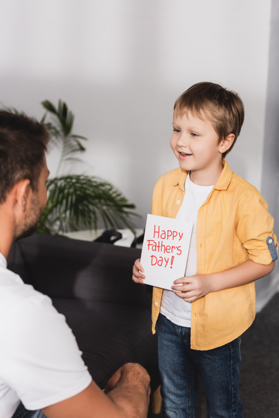 uśmiechnięty chłopiec prezentuje szczęśliwy ojcowie dzień kartka z życzeniami do ojca - Zdjęcie, obraz