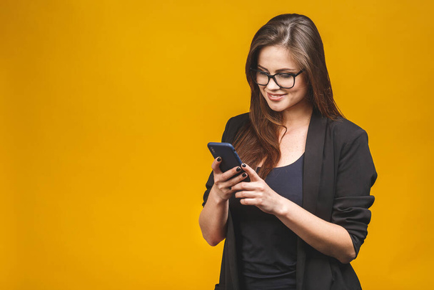 Retrato de una mujer de negocios sonriente en gafas con teléfono inteligente y mirando hacia atrás sobre el fondo amarillo. Usando teléfono
.  - Foto, Imagen