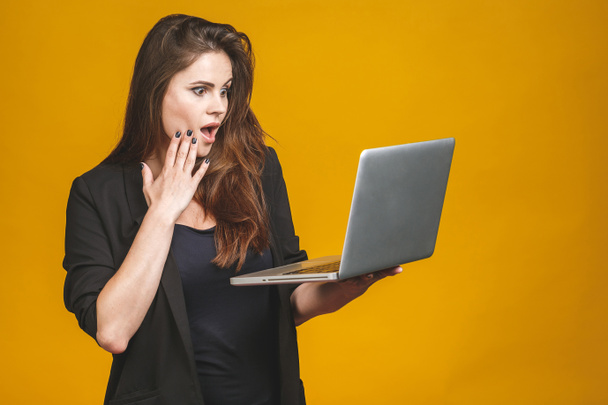 Portrait of happy surprised woman standing with laptop isolated on yellow background. - Photo, Image