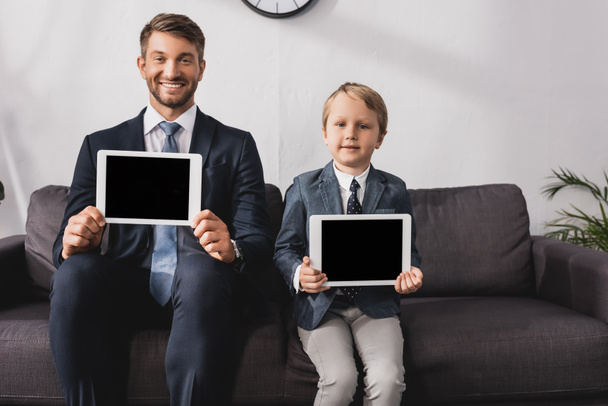 Bonito empresário e filho em desgaste formal mostrando tablets digitais com tela em branco e sorrindo para a câmera
 - Foto, Imagem