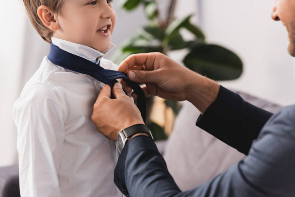 abgeschnittene Ansicht eines Geschäftsmannes, der zu Hause seinem glücklichen, entzückenden Sohn Krawatte anzieht - Foto, Bild