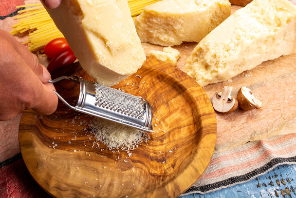 Mann kocht mit italienischem Hartkäse, geriebenem Parmesan oder Grana Padano, Hand mit Käsereibe - Foto, Bild