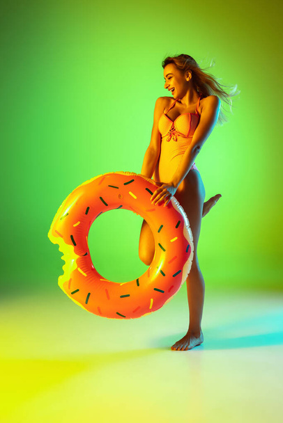 Beautiful girl in fashionable swimsuit isolated on gradient studio background in neon light. Summer, resort, fashion and weekend concept - Фото, изображение