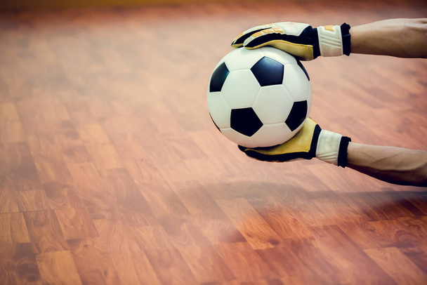Μπάλα στα χέρια του futsal τερματοφύλακα σε ξύλινο futsal πάτωμα. Εσωτερική αίθουσα ποδοσφαίρου. Ποδόσφαιρο futsal παίκτης, μπάλα, Αθλητισμός φόντο. Φούτσαλ πρωτάθλημα νέων. Εσωτερική ποδοσφαιριστές - Φωτογραφία, εικόνα