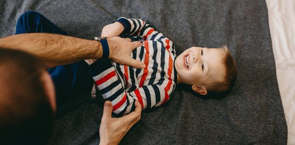 Père caucasien jouant avec son fils sur le canapé couché et souriant à la caméra - Photo, image