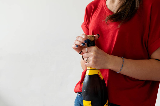 une fille ou une femme déroulant une bouteille de vin mousseux pour une occasion spéciale. Fond blanc pour le texte et pour faire une carte postale. - Photo, image