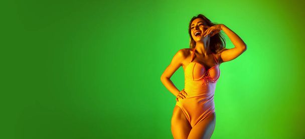 Beautiful girl in fashionable swimsuit isolated on gradient studio background in neon light. Summer, resort, fashion and weekend concept - Foto, Imagen