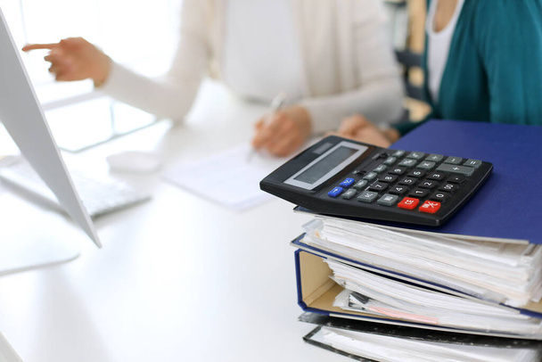Calculator and binders with papers are waiting to be processed by business woman or bookkeeper working at the desk in office back in blur. Internal Audit and tax concept - Foto, imagen