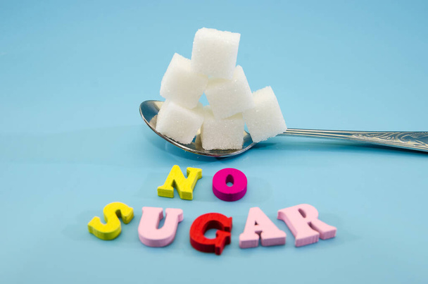 no sugar text word. Concept Diabetes Prevention.White sugar cubes in a spoon on a blue background. Sugar harm concept. - Photo, Image