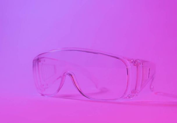 Protective transparent glasses in studio neon pink light. Minimalism. - 写真・画像