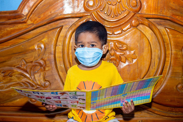 Мальчик в маске и сидит на кровати и читает книгу. Гигиеническая маска для защиты от вирусов. Детский портрет на дому карантин
. - Фото, изображение