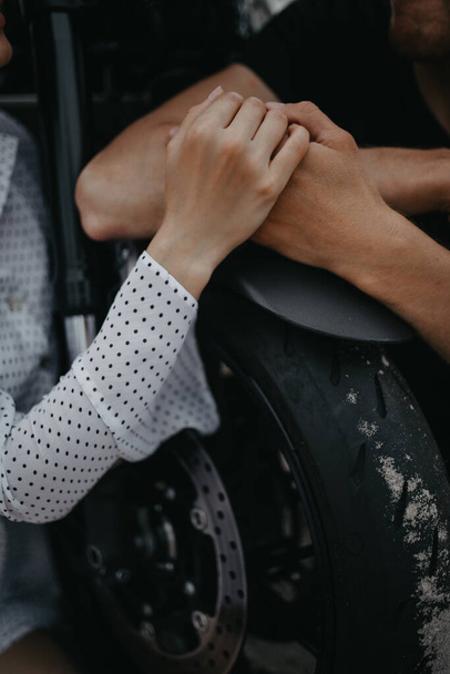Couple sits and holds each other hands on background of wheel motorcycle. Closeup. - Foto, Bild