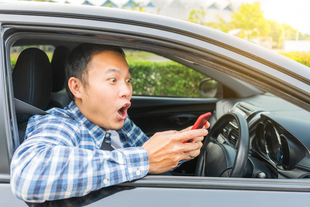 Impresionado y sorprendido guapo asiático hombre mirando smartphone en su coche
. - Foto, imagen
