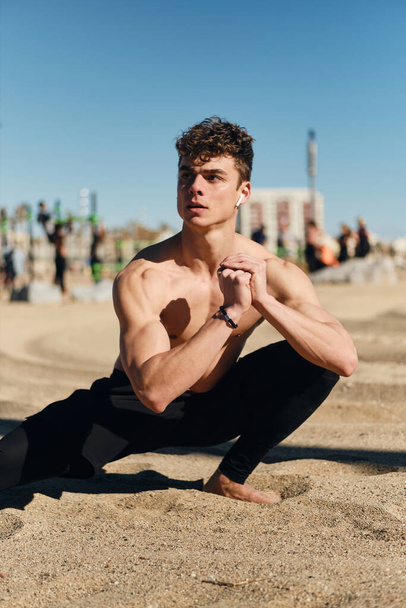 Een jonge sportieve man die zich uitstrekt over het strand van de stad. Knappe fitte jongen op functionele training outdoor - Foto, afbeelding