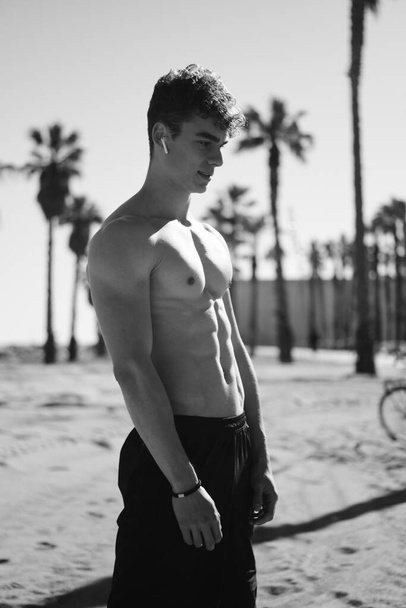 Bel ragazzo sportivo con busto nudo che riposa durante l'allenamento nella calda giornata estiva sulla spiaggia della città. Foto in bianco e nero
 - Foto, immagini