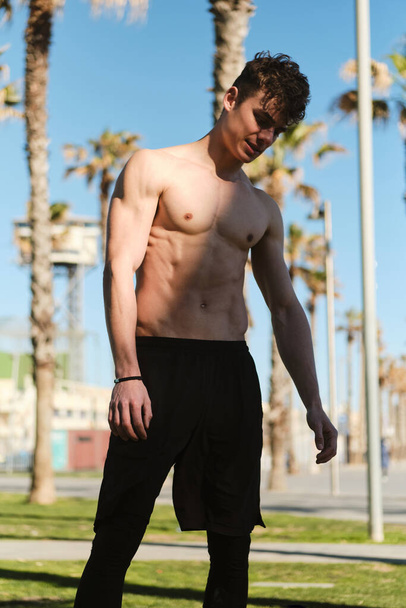 Attractive sporty guy resting after morning run along city beach. Young attractive man on workout outdoor - Фото, изображение