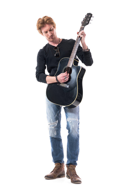 Серйозний крутий молодий красивий гітарист, який грає на гітарі, використовує пік, тримає його вертикально. Повна довжина тіла ізольована на білому тлі
.  - Фото, зображення