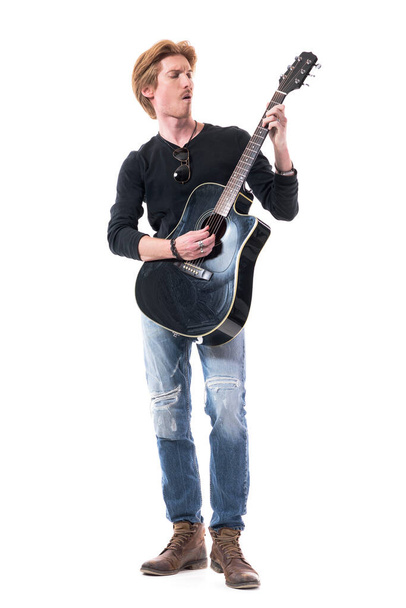 Виразний пристрасний рок-гітарист грає на акустичній гітарі з закритими очима. Повна довжина тіла ізольована на білому тлі
.  - Фото, зображення
