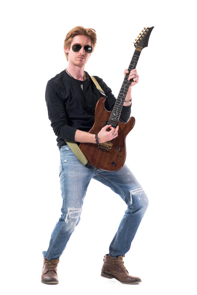 Gepassioneerde stoere rock gitarist speelt elektrische gitaar met vertrouwen. Volledige lichaamslengte geïsoleerd op witte achtergrond.  - Foto, afbeelding