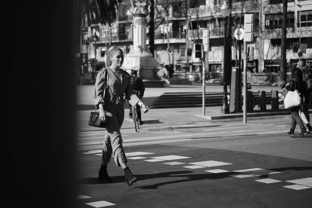 Junge hübsche Frau überquert selbstbewusst die Straße entlang der Stadtstraße. Schwarz-Weiß-Foto - Foto, Bild