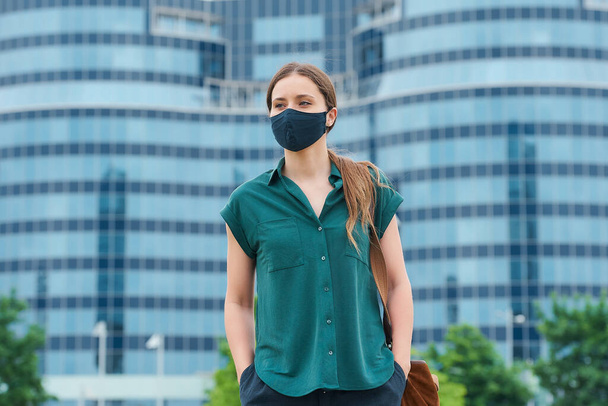 Женщина в медицинской маске для лица, засовывающая руки в карманы брюк в центре города. Девушка держит социальную дистанцию носит защитную маску для лица, чтобы избежать распространения коронавируса
 - Фото, изображение