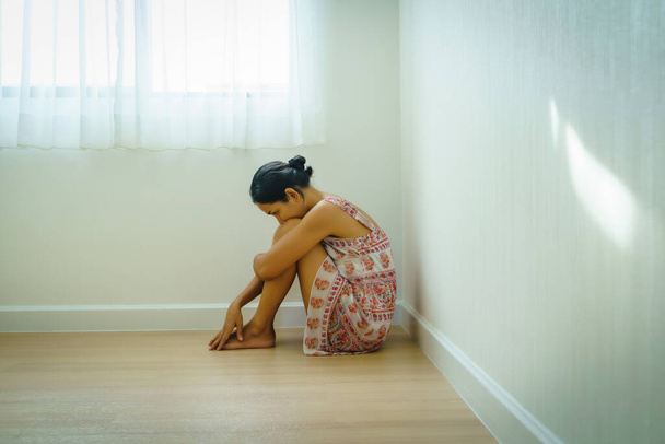 Депресія молодої азіатки сидить на самоті і переслідує її коліна в кутку будинку. Відчайдушний, депресивний розлад або концепція смутку
. - Фото, зображення