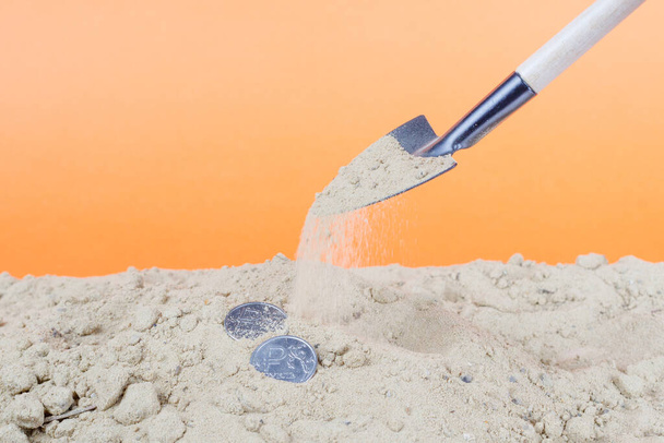 dois rublos metálicos na areia são enterrados na areia com uma pá. areia traz rublo
 - Foto, Imagem
