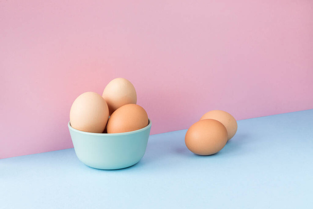 Minimalist image of several brown eggs in a bowl on a light blue and pink background. Copy space available. - Foto, afbeelding