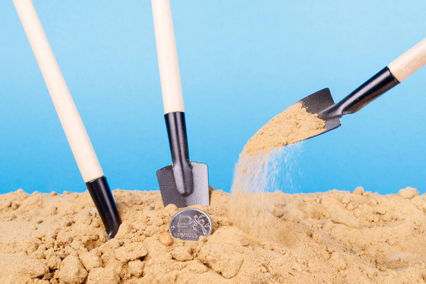 three shovels in the sand, one of them is filling a coin with sand. sand spilling process - Zdjęcie, obraz