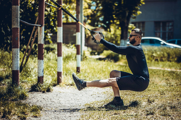 Man doet push-ups oefening met trx fitness riemen. Outdoor, workout, training, lifestyle concep. - Foto, afbeelding