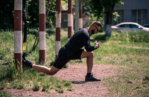Man doing push ups exercise with trx fitness straps. Outdoor, workout, training, lifestyle concep. - Photo, Image