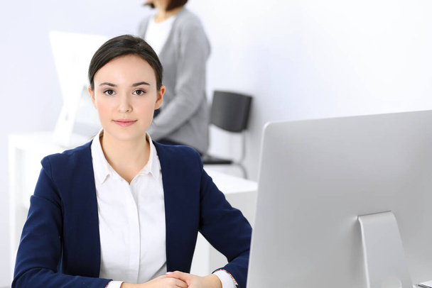 Business woman working with computer in office, female colleague at background. Headshot of Lawyer or accountant at work while sitting at the desk - 写真・画像